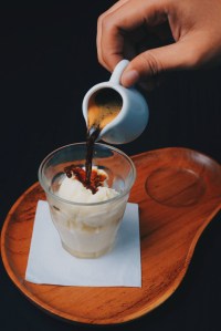a hand pour espresso from a tiny pitcher into a small dish of vanilla ice cream - an affogato